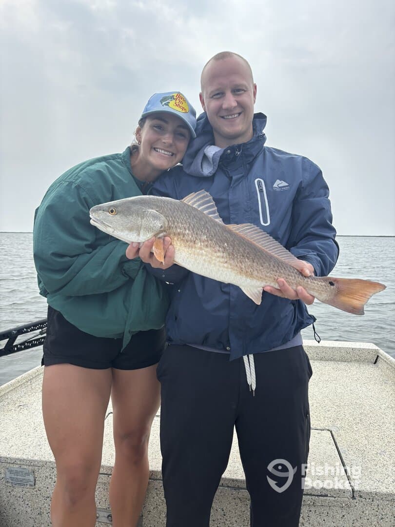 A couple proudly displaying a Redfish while fishing on a boat, showcasing their successful catch during a coastal fishing trip.