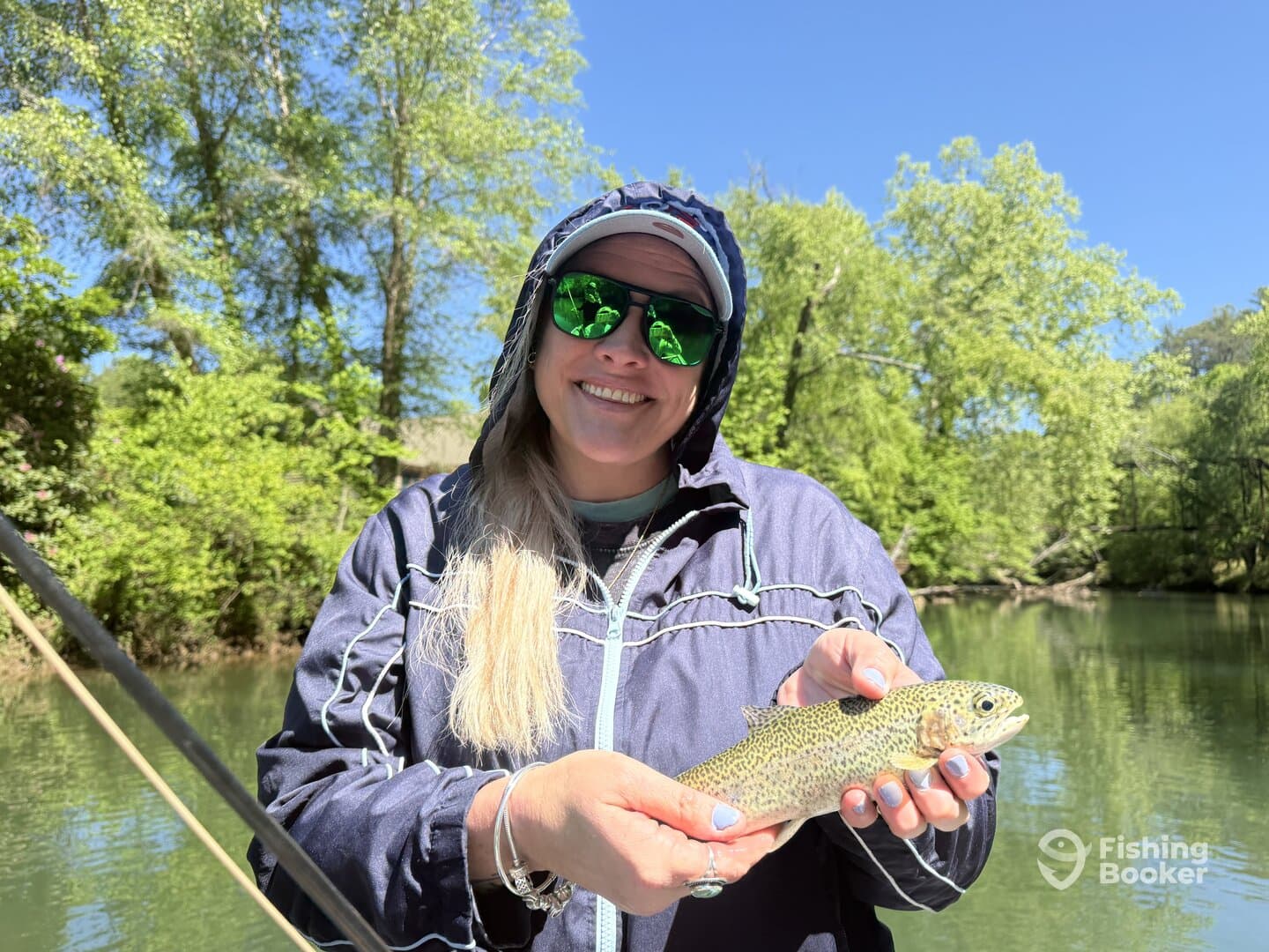 A smiling angler proudly displaying a freshly caught Rainbow Trout while fishing in a serene river setting.