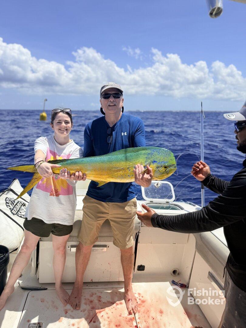 A proud duo displaying a vibrant Mahi Mahi on a fishing charter in open waters, showcasing a successful day of fishing.