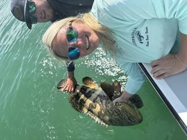 Two anglers proudly displaying a large Goliath Grouper while fishing in clear waters.