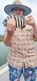 A young angler proudly displaying a striped Sheepshead fish while fishing from a boat.