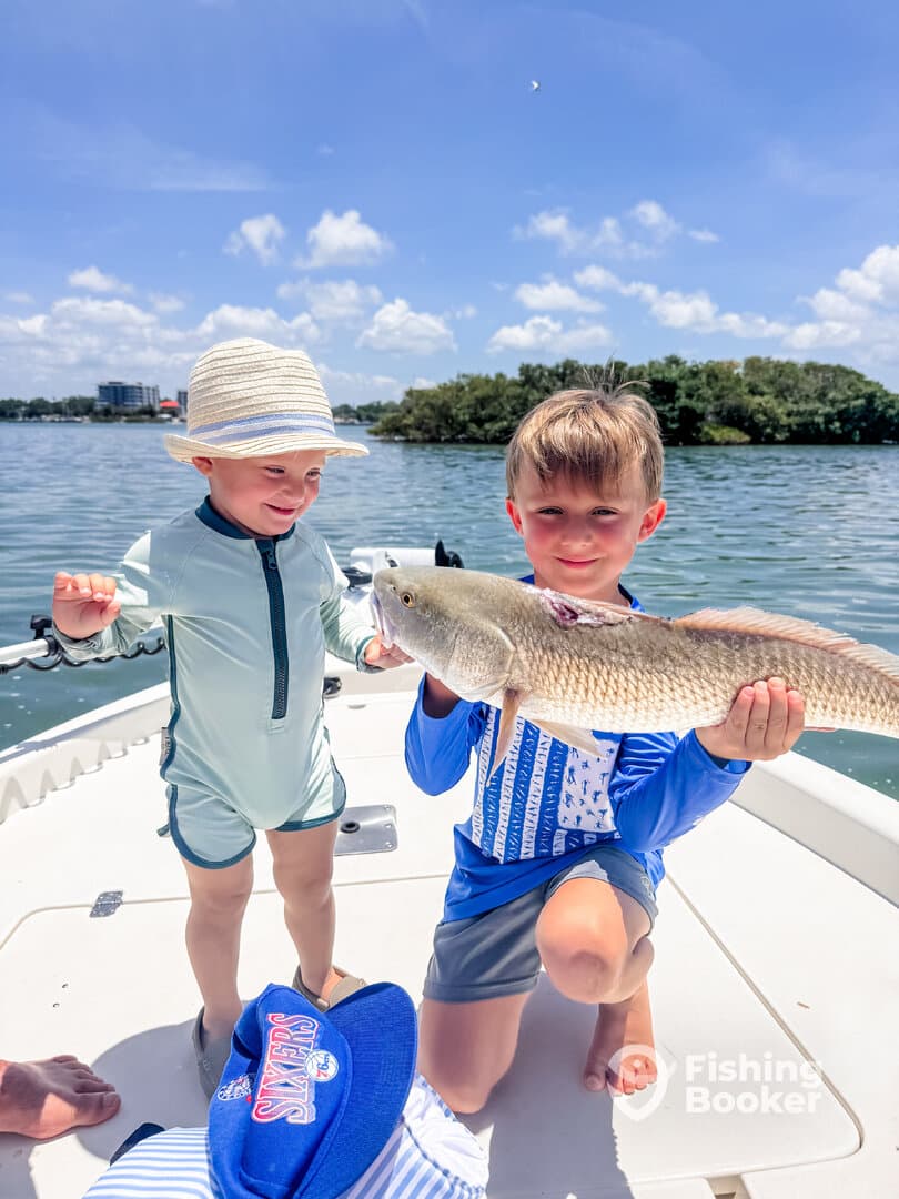 Two young anglers proudly displaying a large Redfish while enjoying a sunny day on the water.