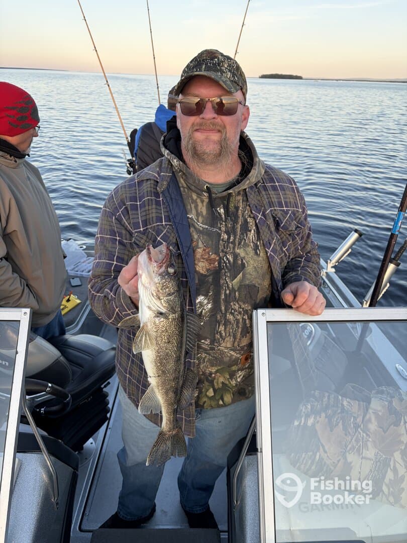 Angler proudly displaying a Walleye while fishing on a boat, surrounded by fellow anglers in a serene lake setting.