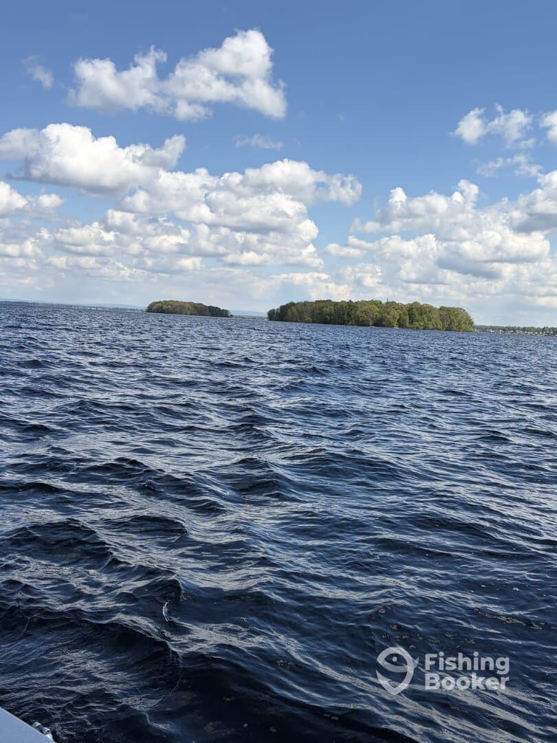 A scenic view of a calm lake with islands in the distance, showcasing a beautiful day for fishing.
