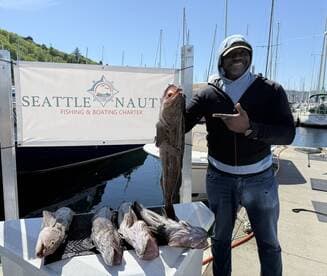A proud angler displaying a large Lingcod alongside several smaller catches at the Seattle Nautical Fishing Charter dock.