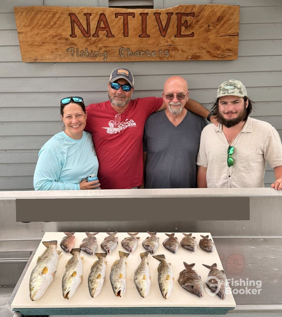 A group of four anglers proudly displaying their catch of various fish, including Speckled Trout, on a board after a successful fishing charter.