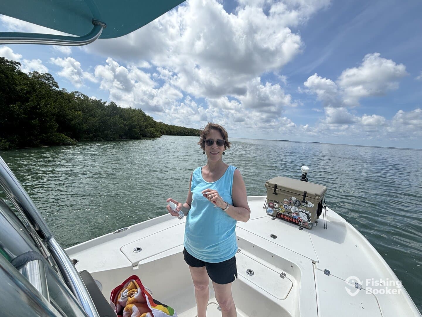 A woman enjoying a sunny day on a boat, surrounded by mangroves, with a cooler and towels visible on board.