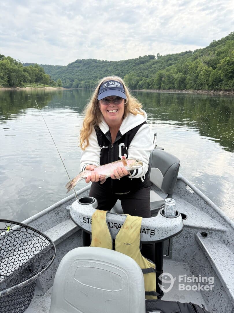 A happy angler proudly displaying a freshly caught Rainbow Trout while fishing on a serene river in Arkansas.