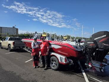 Two anglers posing in front of a red Ranger boat at a marina, showcasing the boat's exterior and nearby vehicles.