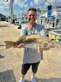 A proud angler displaying a large Grouper caught at the dock, showcasing a successful fishing trip.