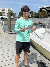 Young angler proudly holding a large fish at the dock, showcasing a successful fishing trip.