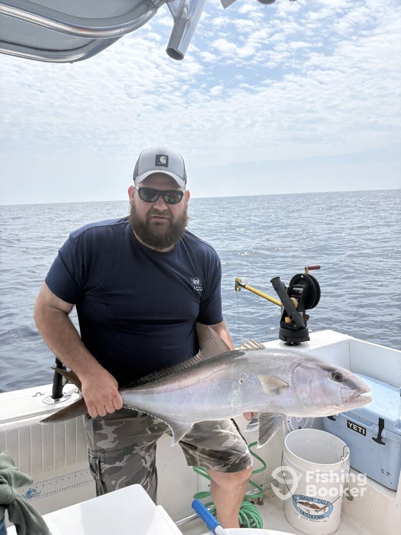 Angler proudly displaying a large Amberjack while fishing offshore, showcasing the excitement of a successful catch.