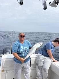 A proud angler holding a large fish on a boat, showcasing a successful fishing trip.