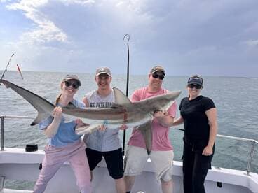 A group of anglers proudly displaying a large shark caught during their fishing trip, showcasing the excitement of deep-sea fishing.