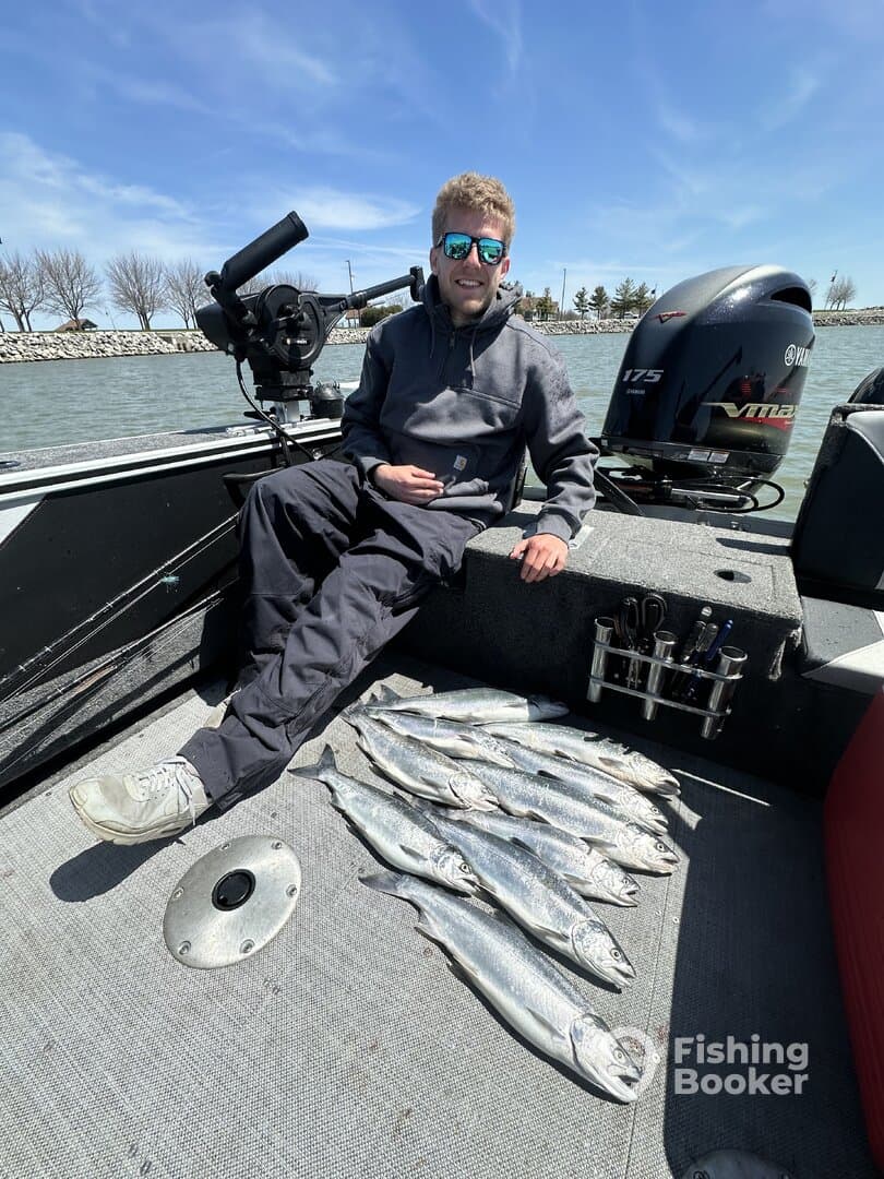 A young angler sits on a boat with a catch of multiple silver fish laid out on the deck, showcasing a successful fishing trip.