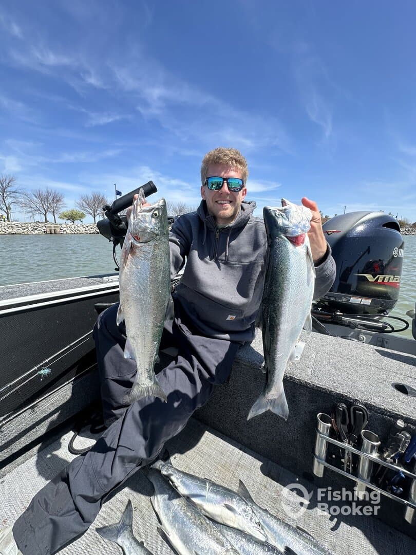 Angler proudly displaying two large Silver Salmon on a fishing boat, with additional fish laid out on the deck.