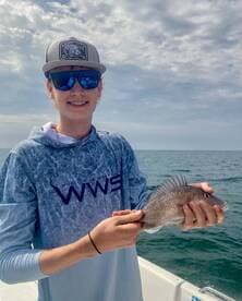 A young angler proudly displaying a Snapper while fishing on a boat in open waters.
