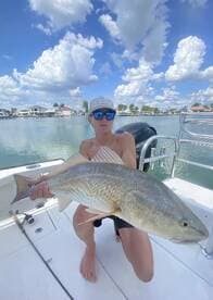 Young angler proudly holding a large Redfish while fishing in a scenic coastal area.