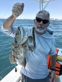 An angler proudly displaying a large Grouper caught while fishing offshore, showcasing the excitement of a successful day on the water.