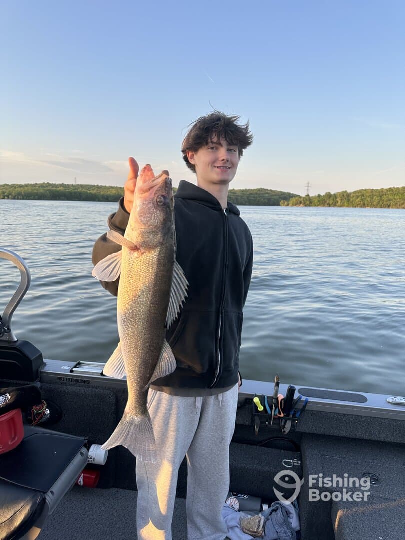 A young angler proudly displaying a large Walleye while fishing on a calm lake, showcasing a successful catch.