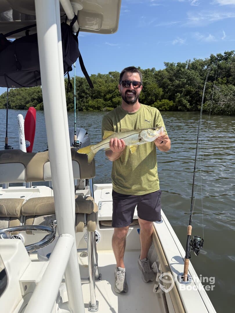 Angler proudly displaying a Snook caught while fishing from a boat in a scenic waterway.