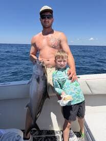 A proud young angler and an adult display a large fish on a sunny day out at sea, showcasing a memorable fishing experience.