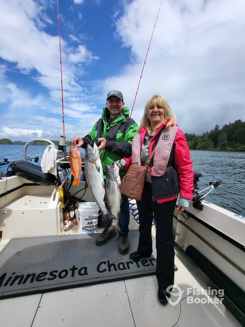Two anglers proudly displaying their catch, including a large salmon and a rockfish, aboard a charter boat in a scenic fishing environment.