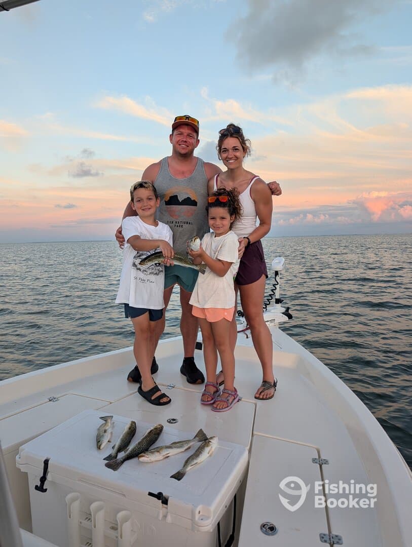 A family proudly displaying their catch of Speckled Trout on a boat during a sunset fishing trip.