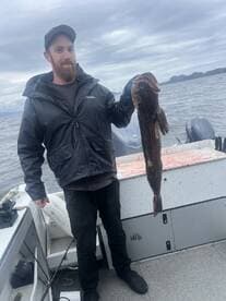 Angler proudly displaying a large Lingcod while fishing on a boat in open waters.