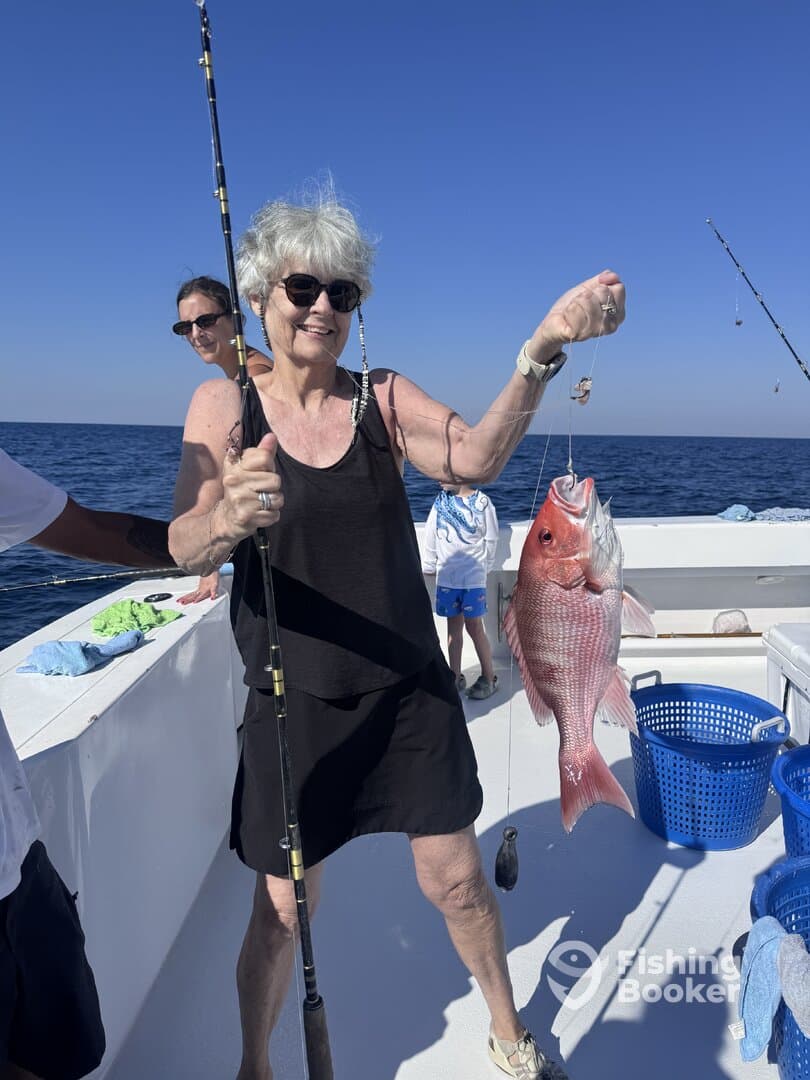A proud angler holding a large Red Snapper while fishing on a charter boat, enjoying a sunny day at sea.