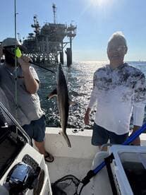 Two anglers proudly displaying a caught shark while fishing near an offshore oil rig.