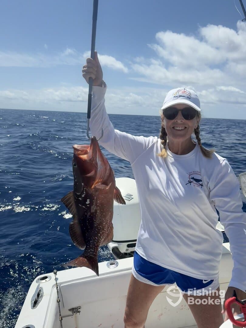 A proud angler holding a large Grouper while fishing on a sunny day in open waters.