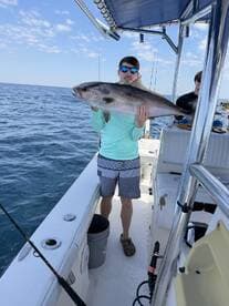 A young angler proudly displaying a large fish while fishing on a boat in open water.