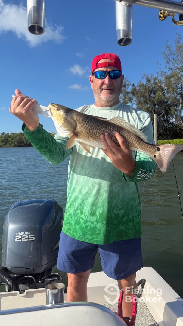 Angler proudly displaying a Redfish while fishing on a boat in a scenic waterway.