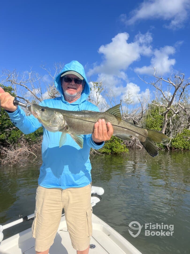 An angler proudly displaying a large Snook while fishing from a boat in a scenic coastal environment.