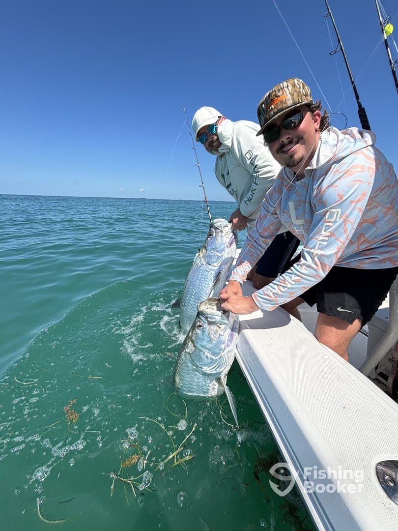 Two anglers proudly displaying their catch of Tarpon while fishing in clear waters, showcasing a successful day on the boat.