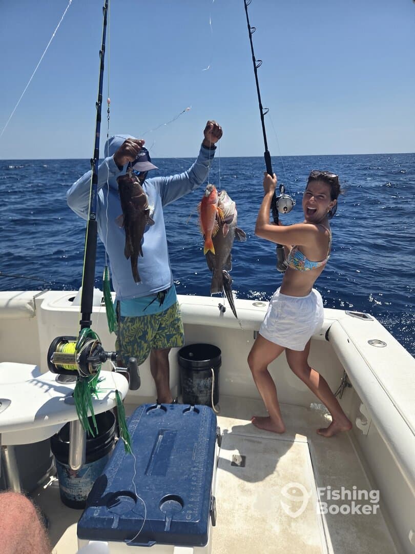 Two anglers celebrating their catch of colorful fish, including a Snapper, while fishing on a sunny day in open waters.