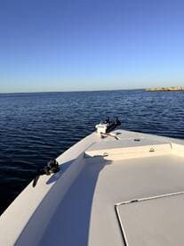 A clear view of the bow of a fishing boat on calm waters, showcasing the boat's design against a serene blue sky.