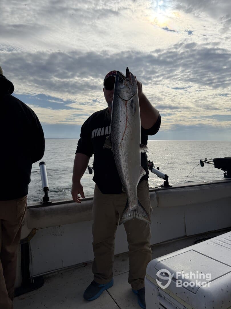 Angler proudly displaying a large Salmon on a fishing boat, with a scenic ocean backdrop.