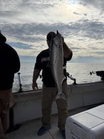 Angler proudly displaying a large Salmon on a fishing boat, with a scenic ocean backdrop.