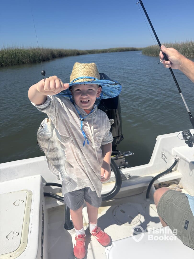 A young angler proudly displaying a caught fish while fishing on a boat in a scenic waterway.