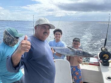 A family proudly displays a large Wahoo caught during their fishing trip, with smiles all around on the boat.