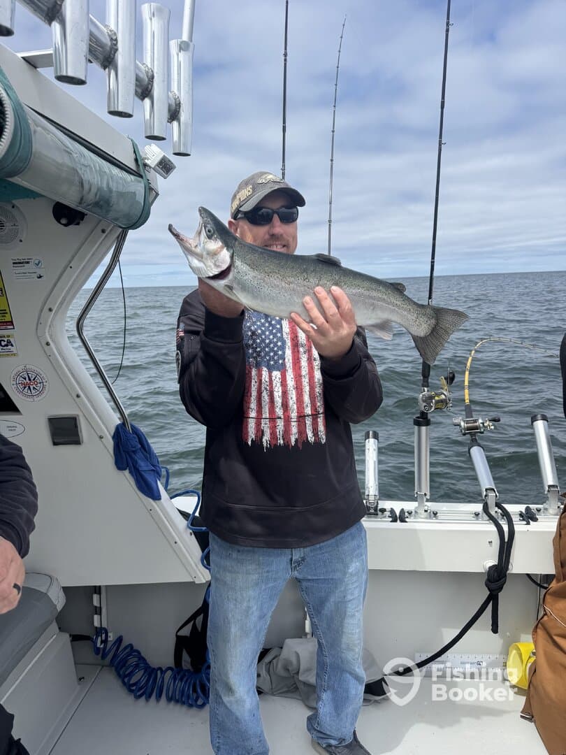 Angler proudly displaying a large trout while fishing on a charter boat, showcasing a successful day on the water.