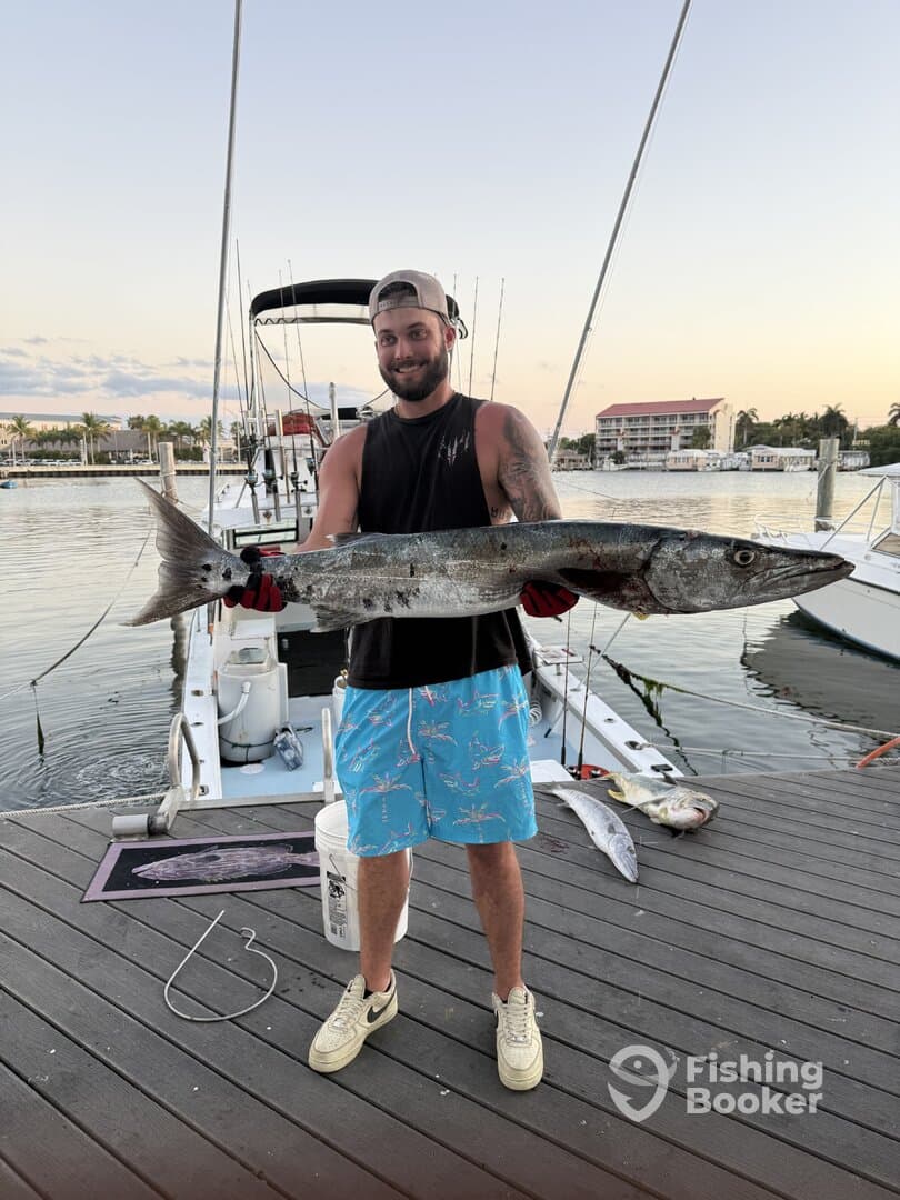 Angler proudly displaying a large Barracuda on the dock after a successful fishing trip.