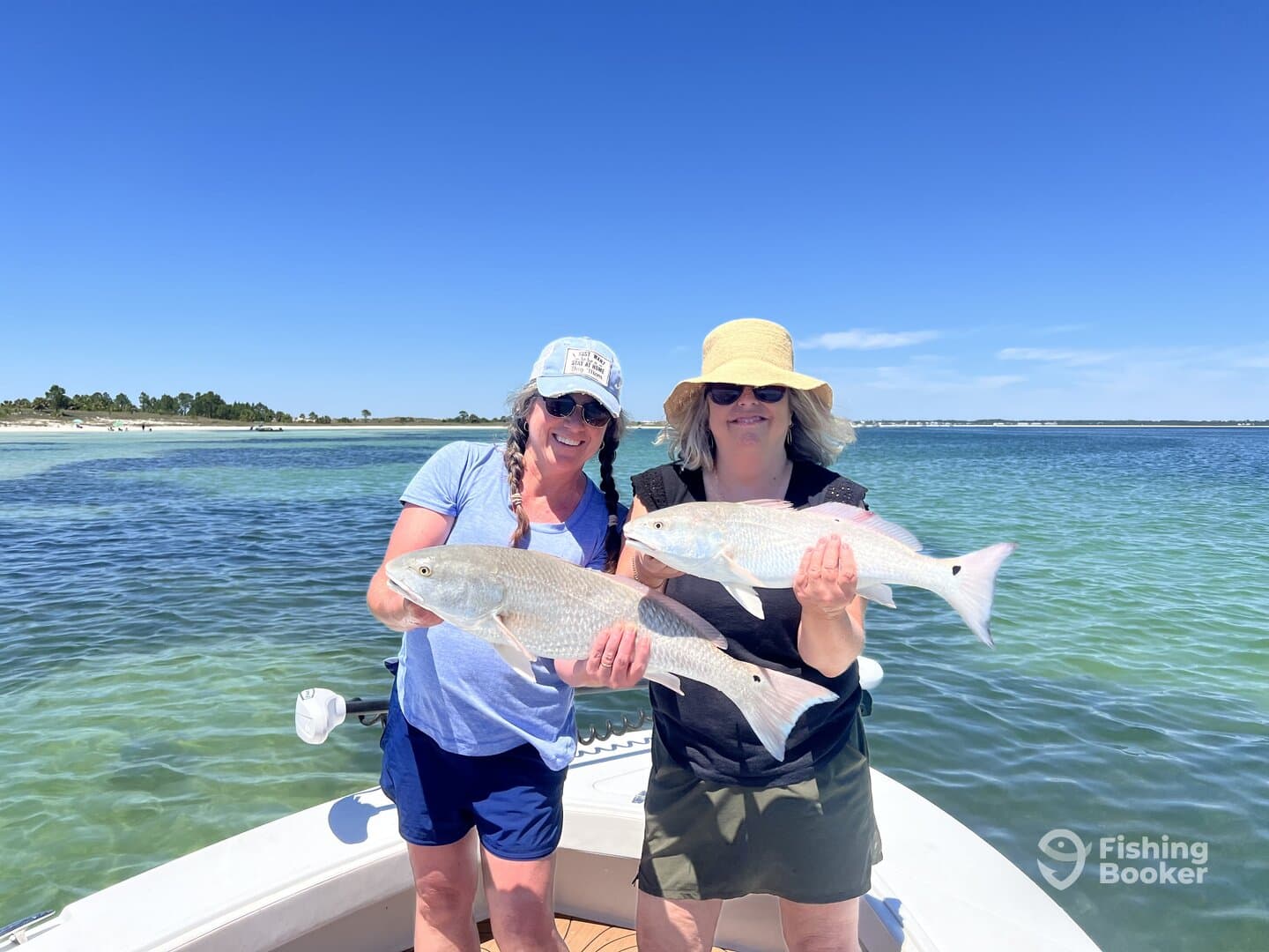 Two women proudly displaying their catch of Redfish while enjoying a sunny day on the water.