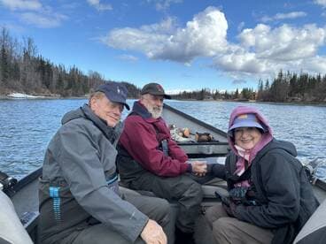Three anglers enjoying a day on the water in a boat, surrounded by a scenic river landscape.