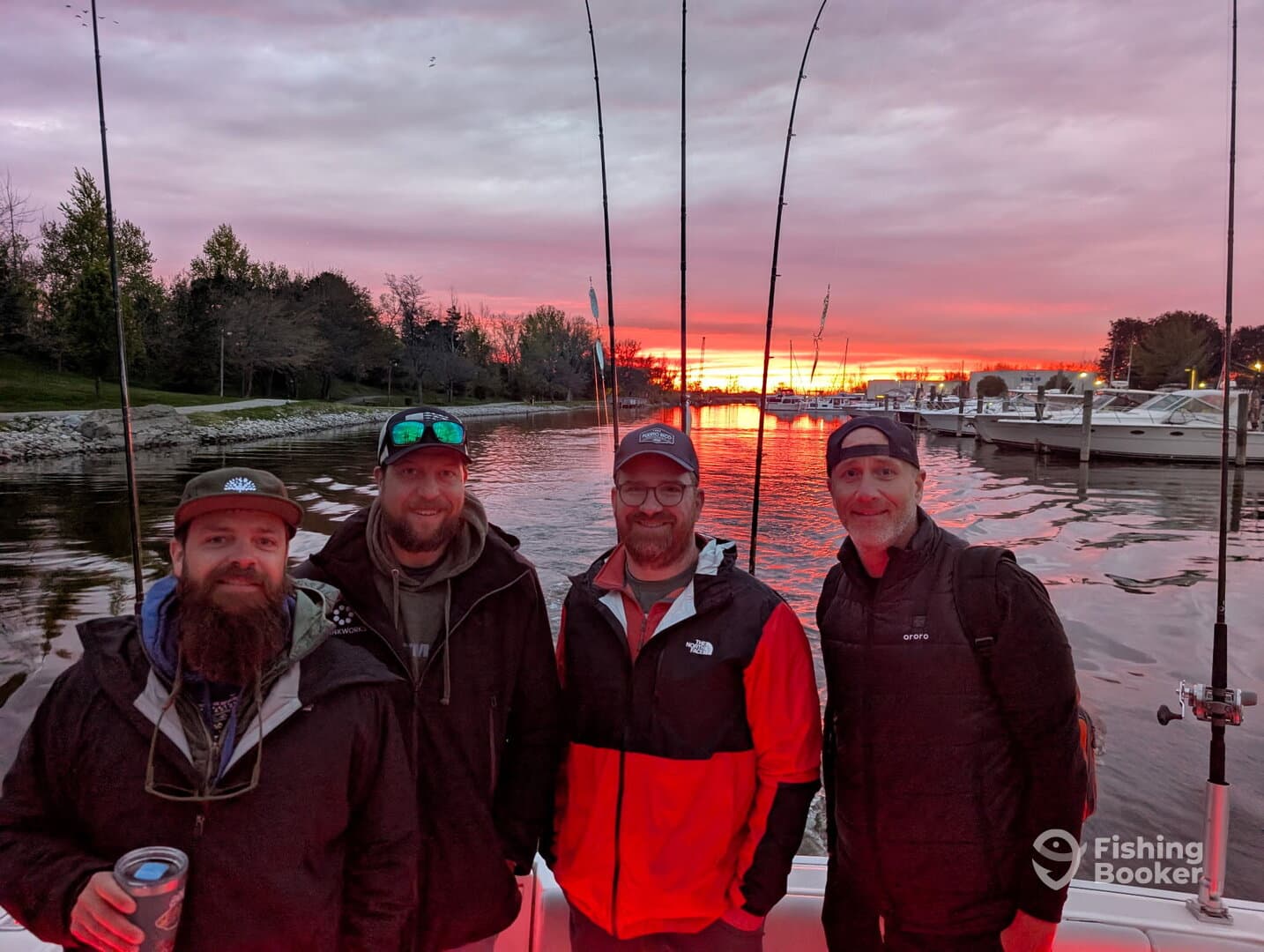 Group of four anglers enjoying a sunset view from their boat, with fishing rods in the background.