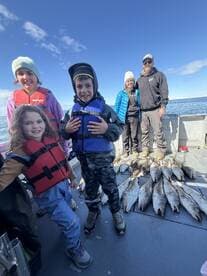 A joyful family of young anglers proudly displaying their catch of multiple fish on a fishing trip, with the scenic ocean backdrop.