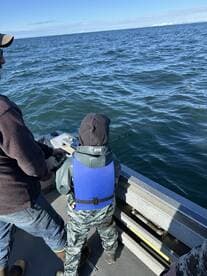 A young angler in a life jacket is actively fishing from a boat, with a clear view of the ocean in the background.