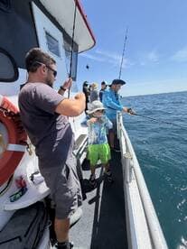 A young angler is actively fishing alongside adults on a charter boat, enjoying a sunny day on the water.